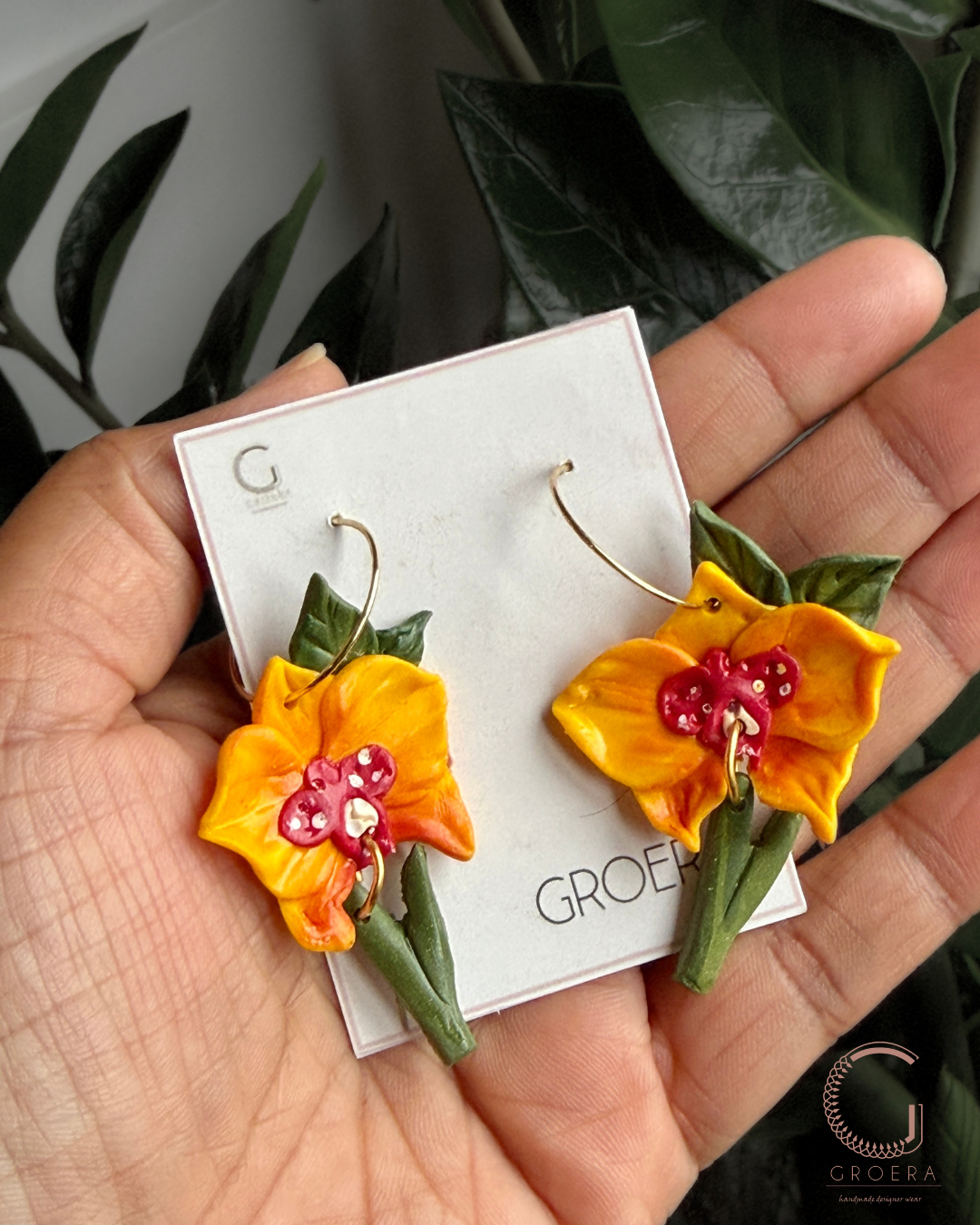 Flower-shaped earrings on aGroea branded card held by a hand with a leafy background.