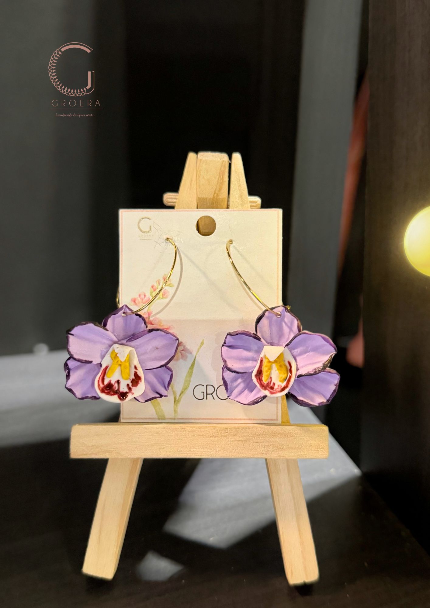 Purple flower earrings on a small wooden easel with 'groera' branding.