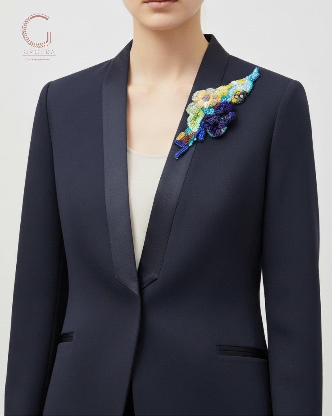 Navy blazer with a colorful floral brooch on a light gray background