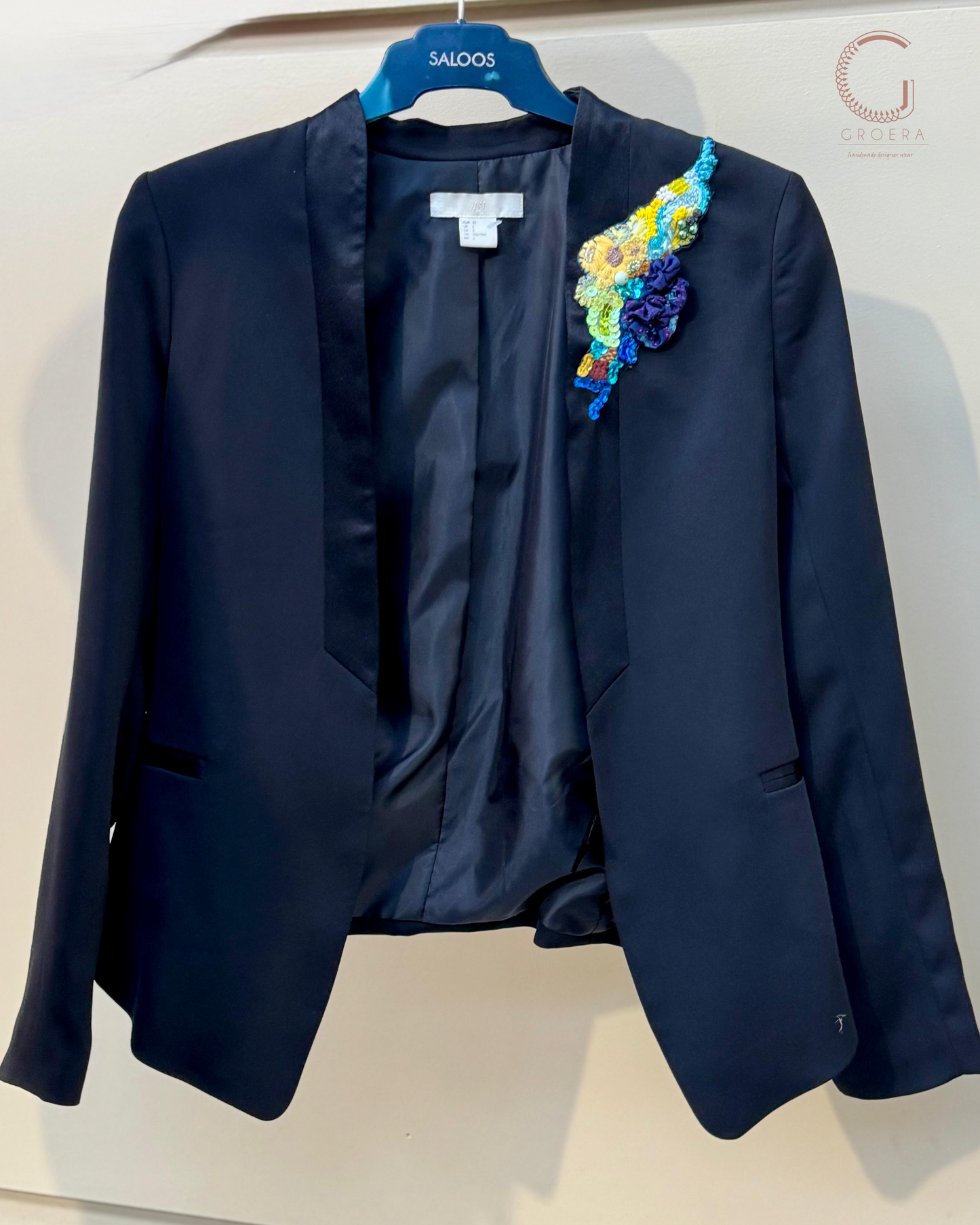 Navy blue blazer with a colorful floral brooch on a white background