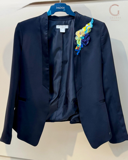 Navy blue blazer with a colorful floral brooch on a white background