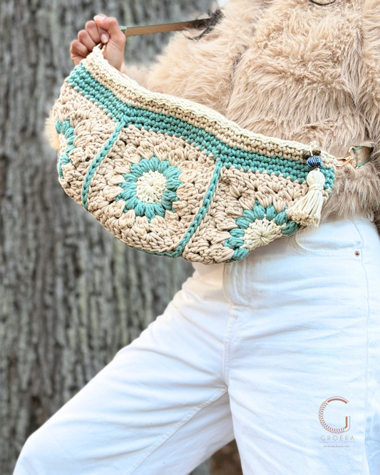 Person holding a crocheted bag with a floral pattern against a tree background