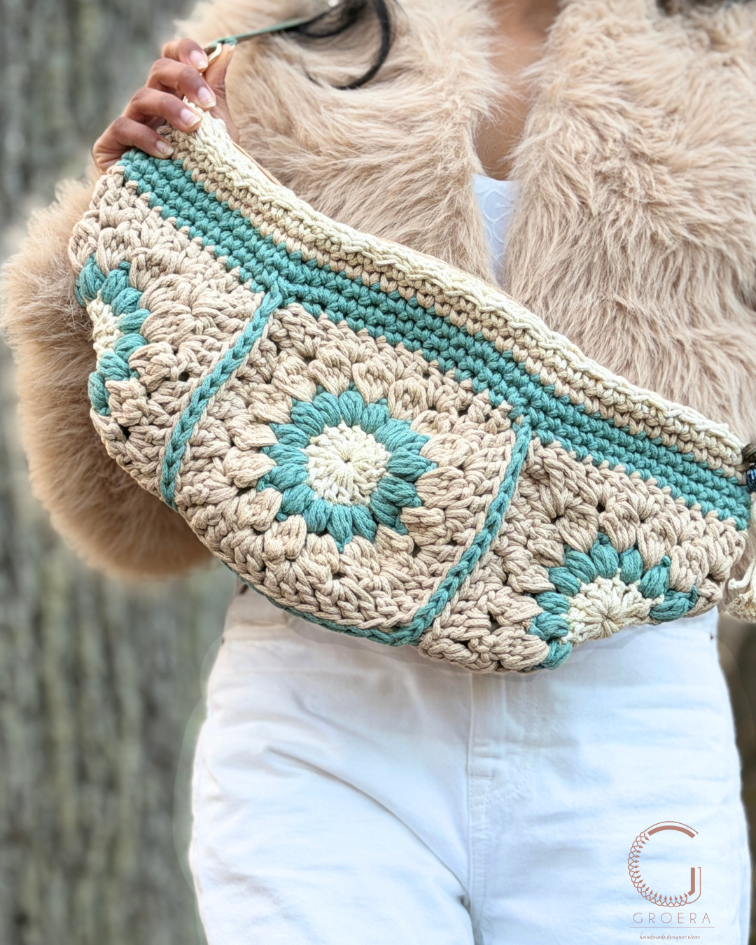 Person holding a crocheted bag with turquoise accents and beige pattern.