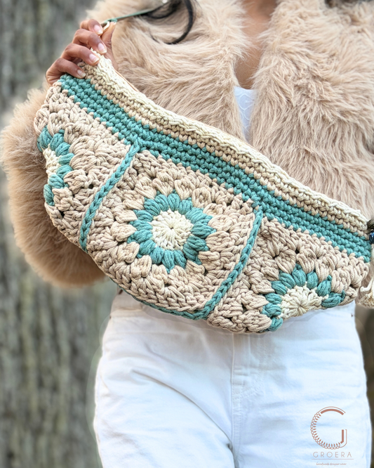 Person holding a crocheted bag with turquoise accents and beige pattern.