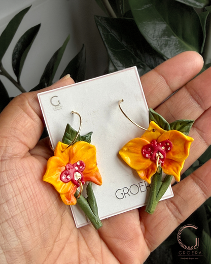 Flower-shaped earrings on aGroea branded card held by a hand with a leafy background.