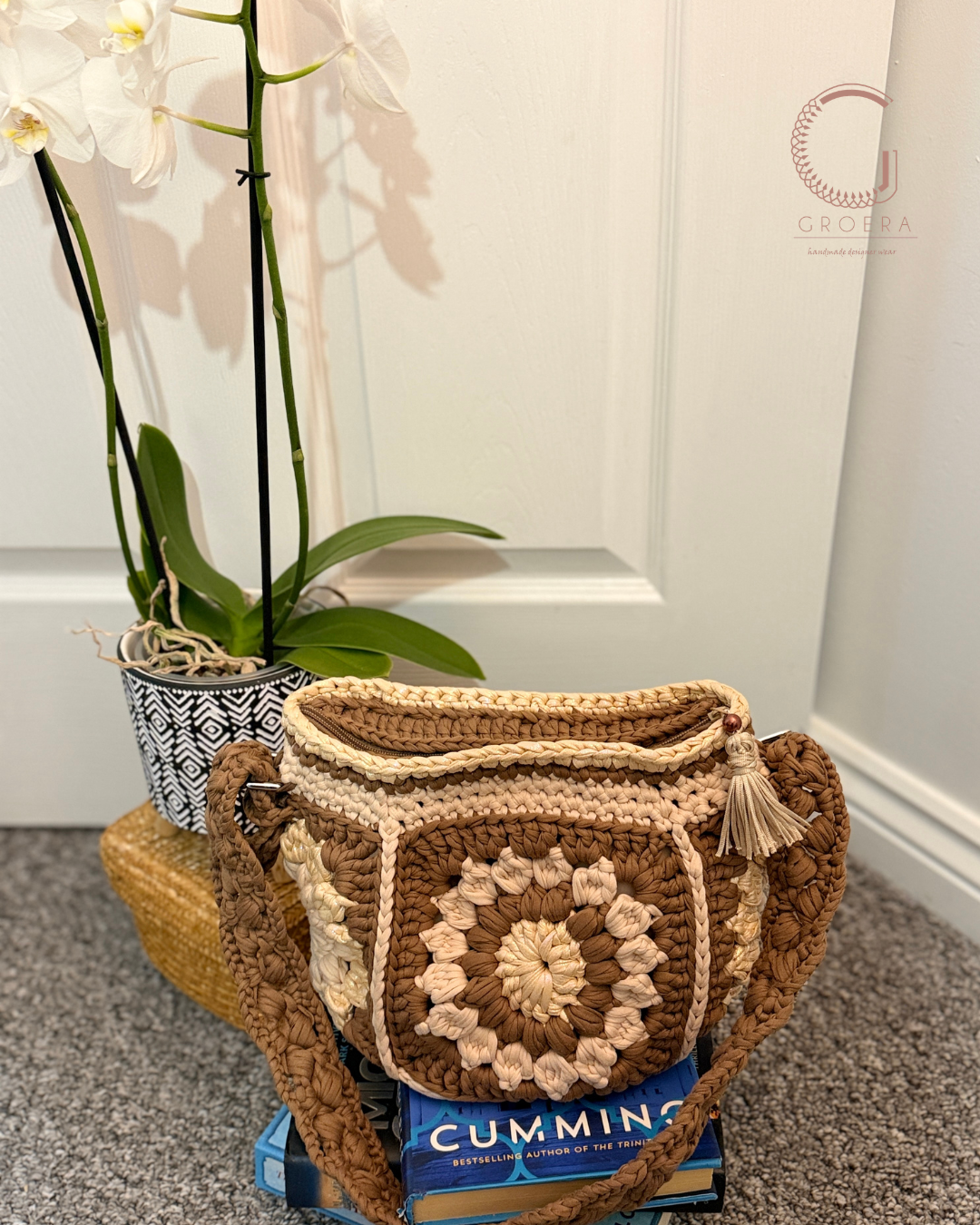 Brown crochet bag with tassels on a box, next to a plant indoors.