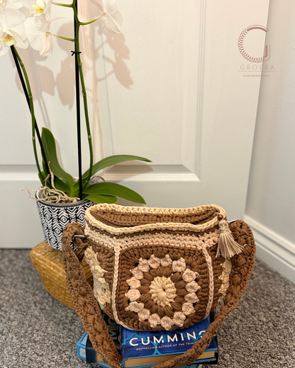 Brown crochet bag with tassels on a box, next to a plant indoors.