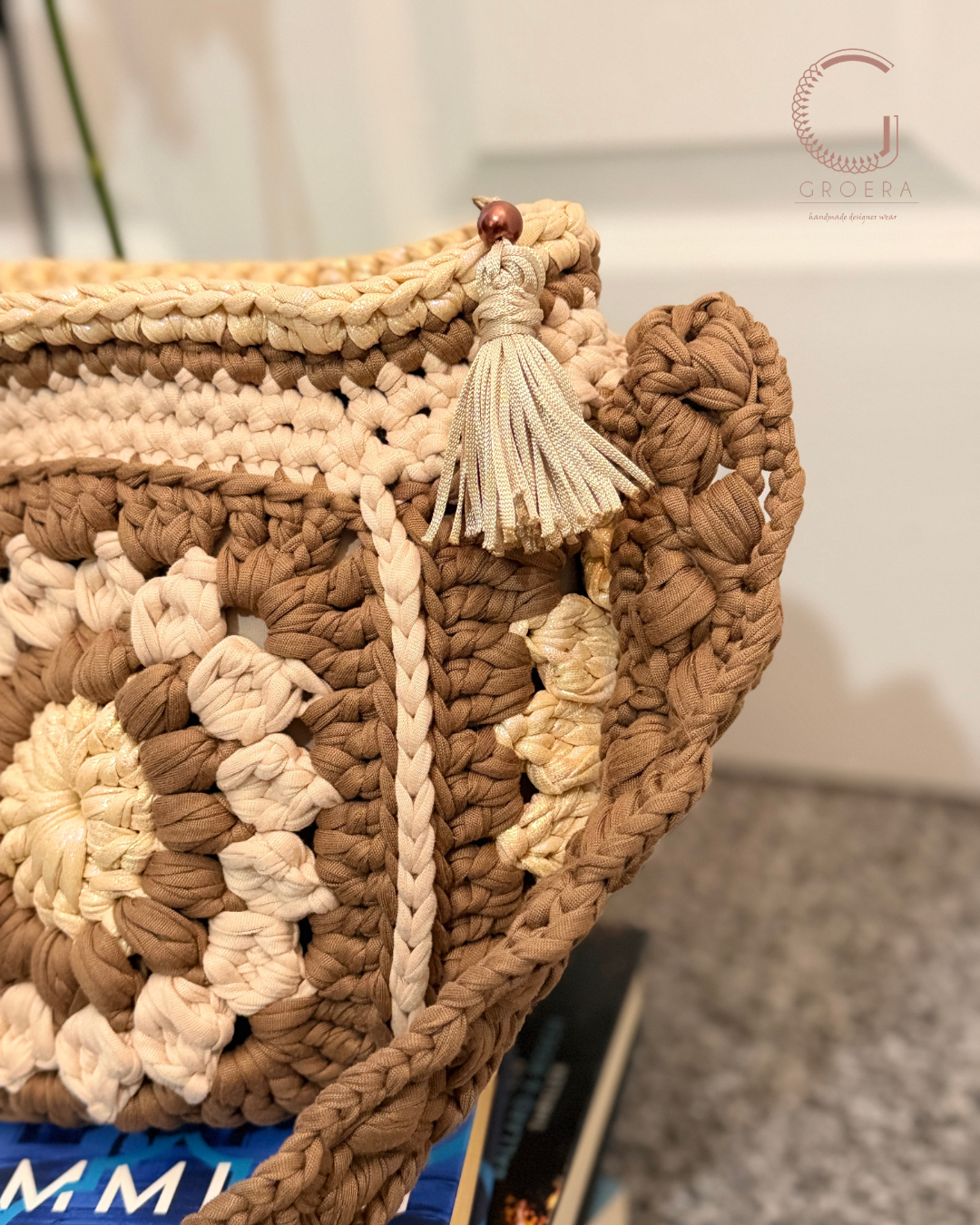 Close-up of a crocheted bag with floral patterns and a tassel, brand 'G' visible.