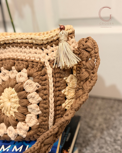 Close-up of a crocheted bag with floral patterns and a tassel, brand 'G' visible.