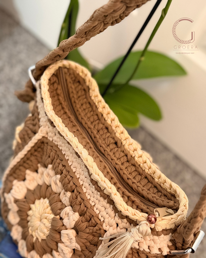 Brown and beige crochet handbag with floral patterns on a blurred background