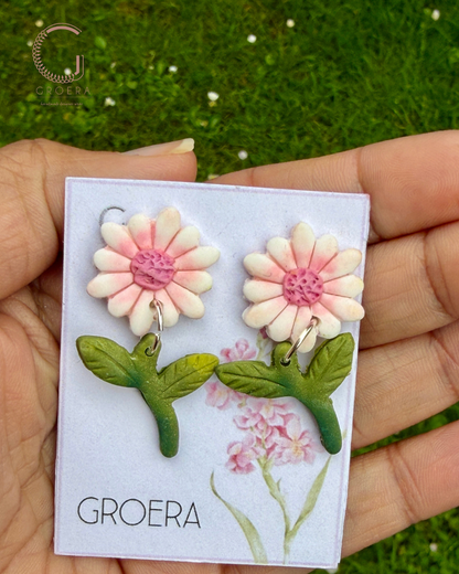 Flower-shaped earrings on a card held by a hand with a green grass background