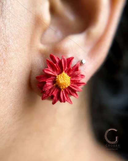 Red flower-shaped earring worn on an ear with a blurred background