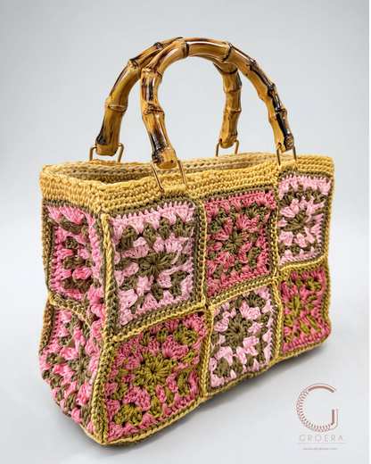 A handmade crocheted bag featuring square granny-square panels in pink, olive green, and beige, with a faux bamboo handle, shown on a light gray background.