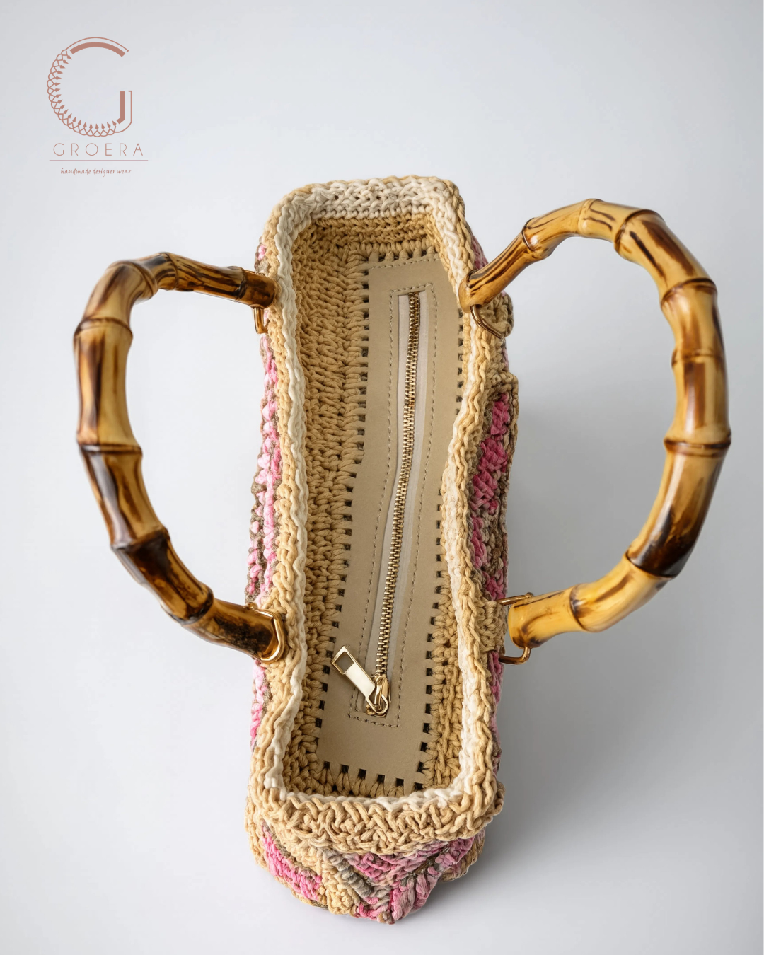 A woven straw and pink yarn handbag with distinctive brown bamboo handles, shown from a top-down view on a light gray background. The brand logo 'G GROERA' is visible in the top left corner.