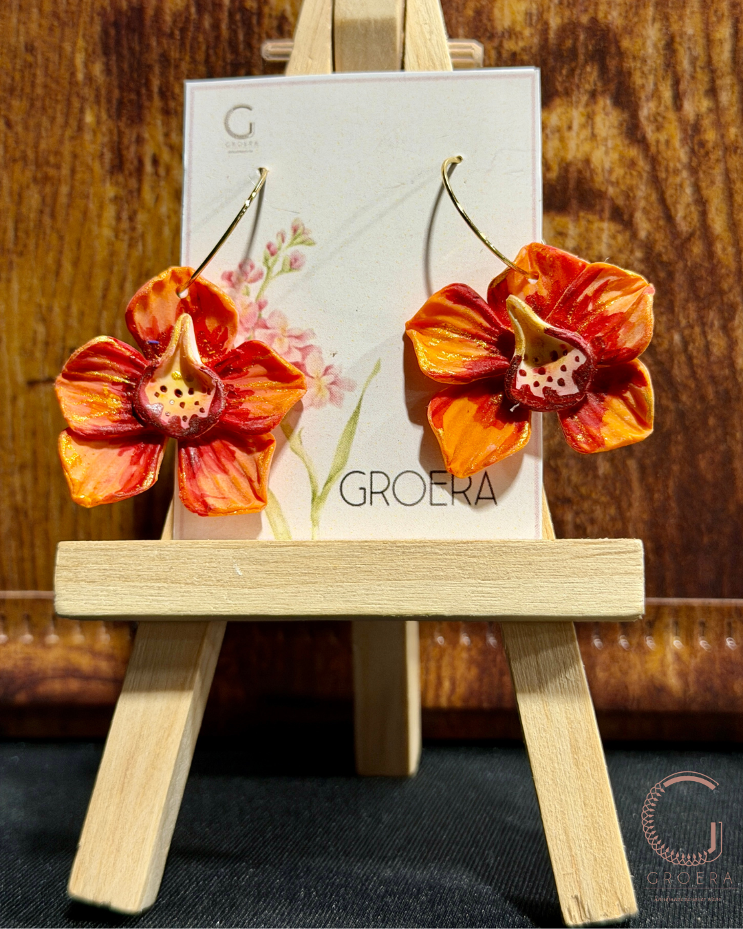 Floral earrings on a small wooden easel with a 'GROERA' card in the background.