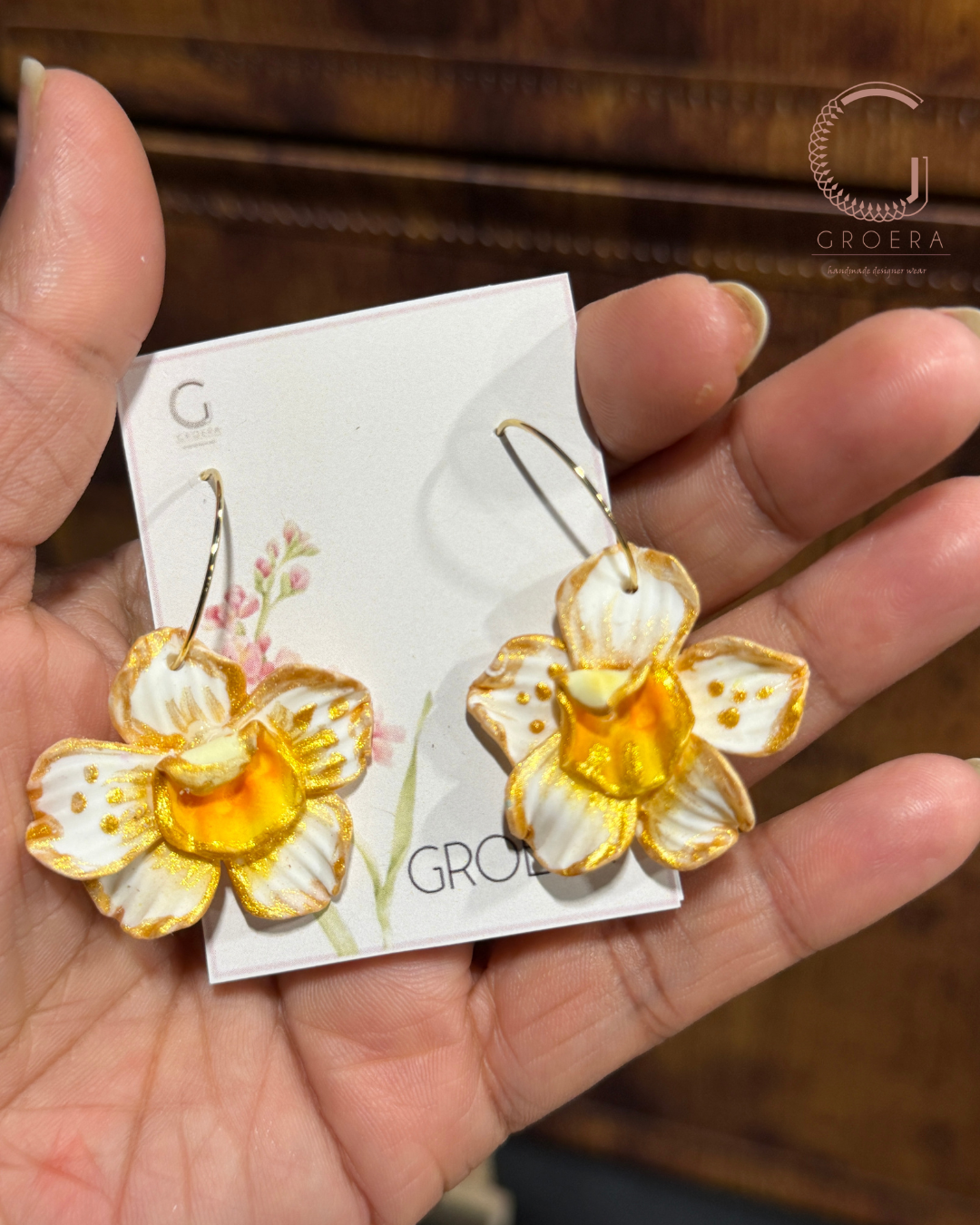 Flower-shaped earrings on a Groera branded card held in a hand.