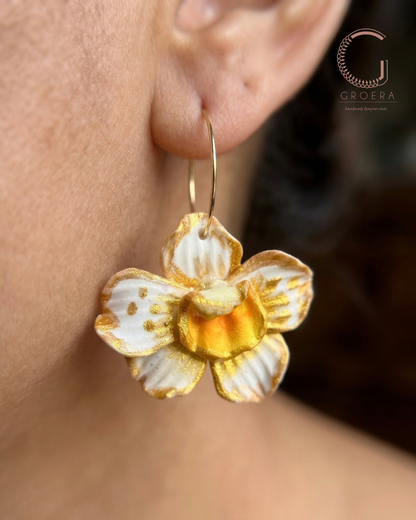 Gold and white floral earring worn by a person, with Groera brand visible.