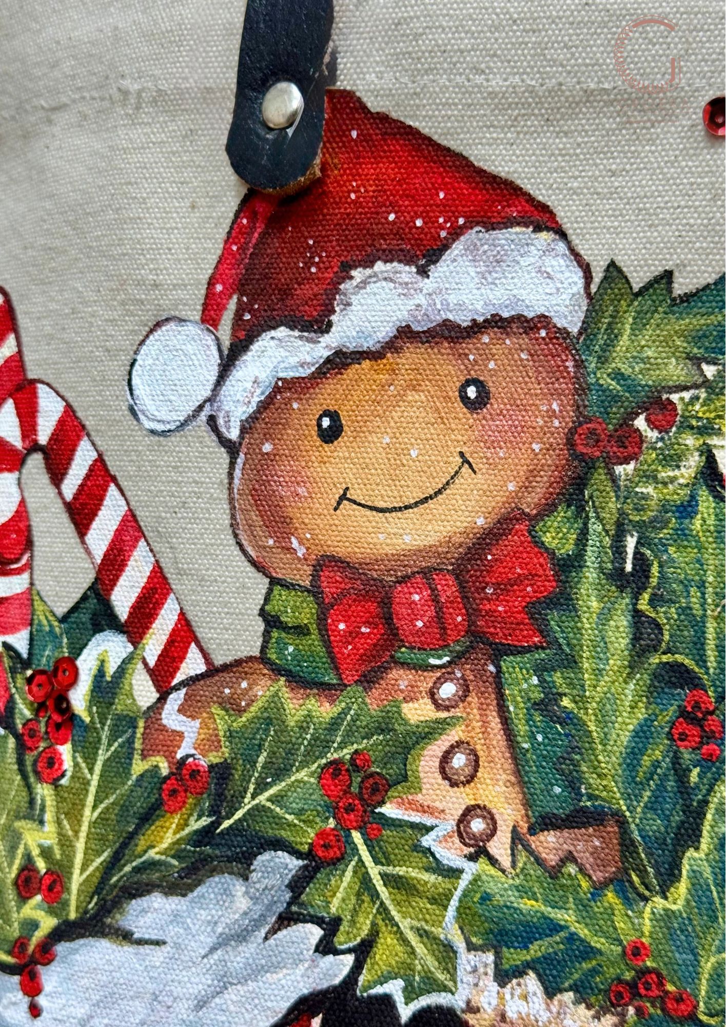 Decorative gingerbread man with a red hat and bow tie surrounded by holly and candy canes on a textured fabric background.