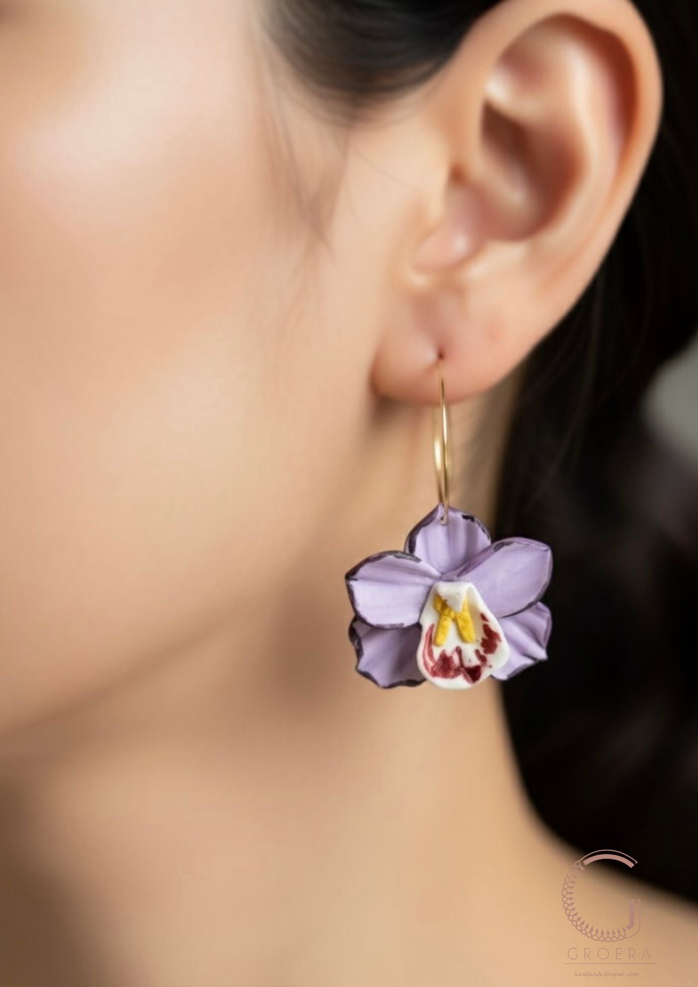 Close-up of a person wearing a purple orchid earring with a blurred background