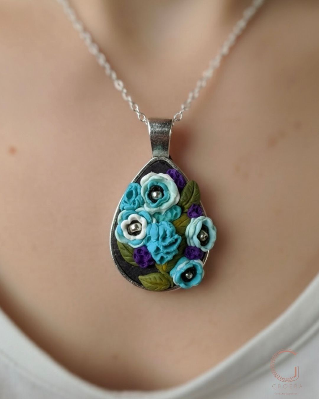 Teardrop-shaped floral pendant necklace on a person wearing a white top.