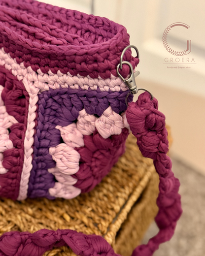 Close-up of a crocheted bag with a pink and purple pattern on a blurred background.