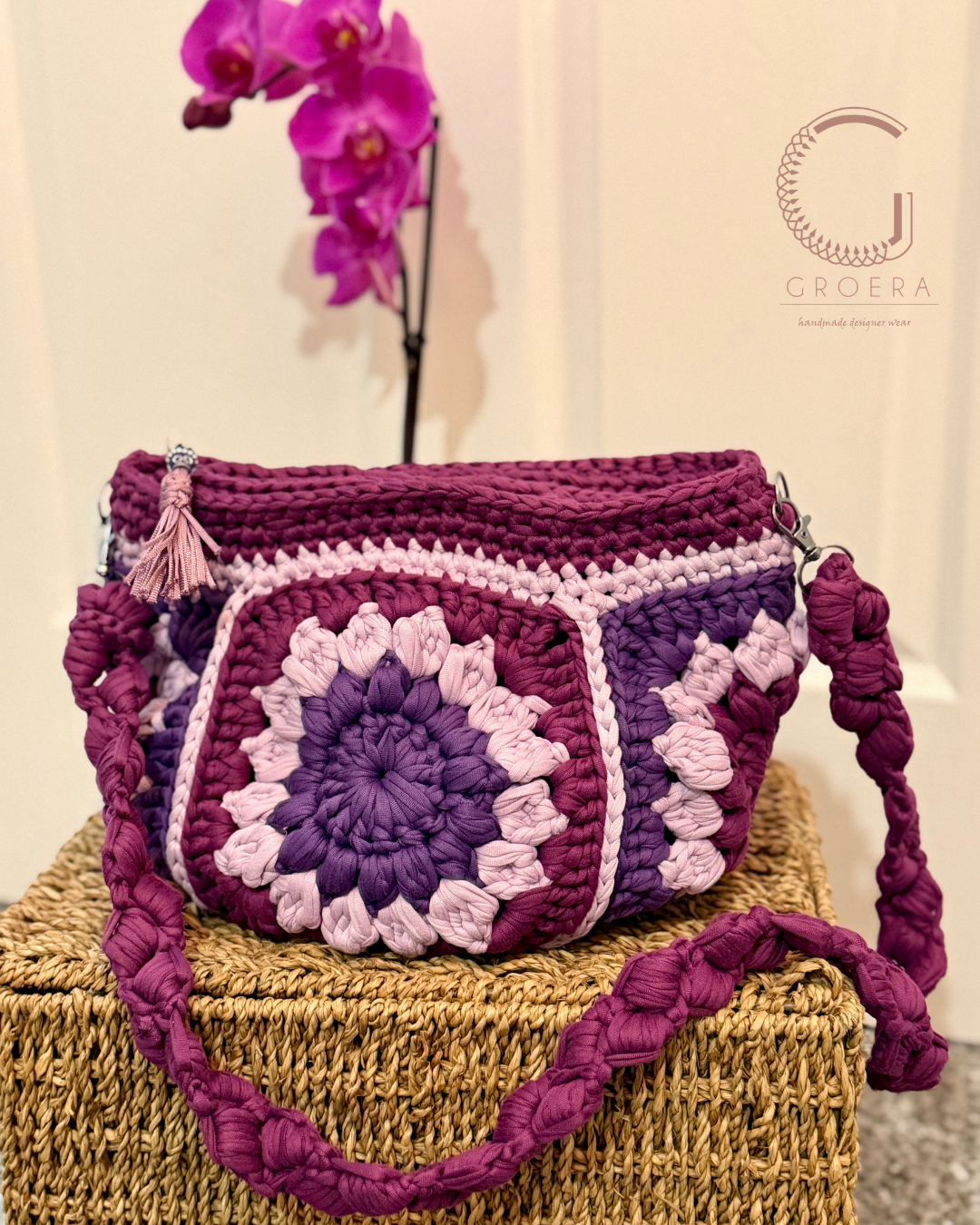 Crocheted handbag with a floral pattern on a textured surface, featuring the brand 'Groera'.