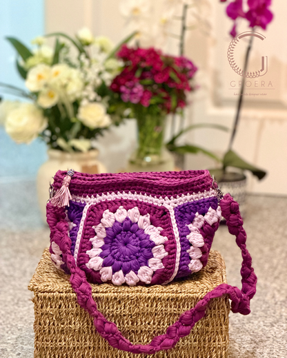 Purple crochet bag with floral patterns on a woven box, flowers in the background